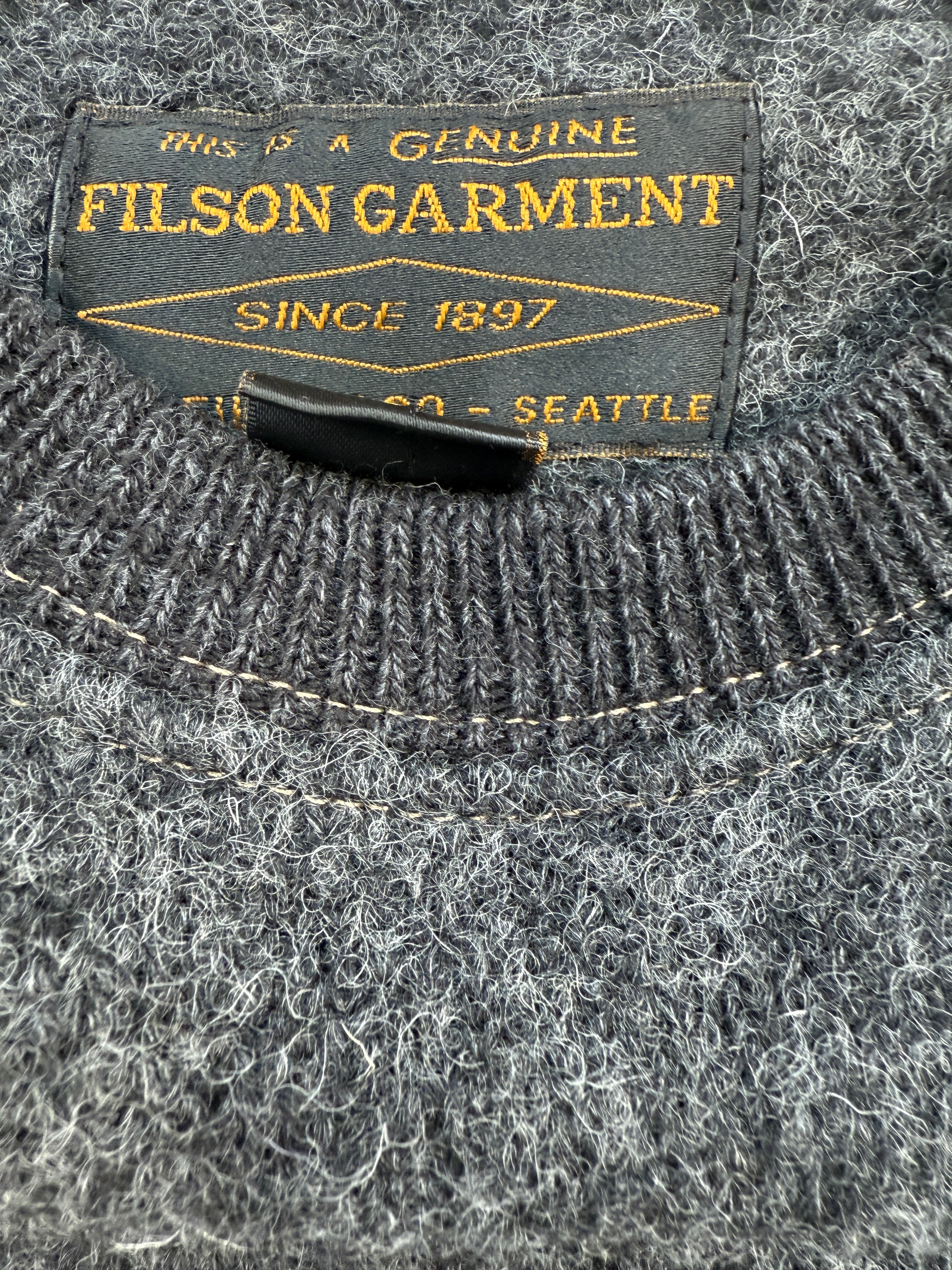 Grey wool sweater by Filson, with a textured, heathered knit and a brand tag visible at the neckline.