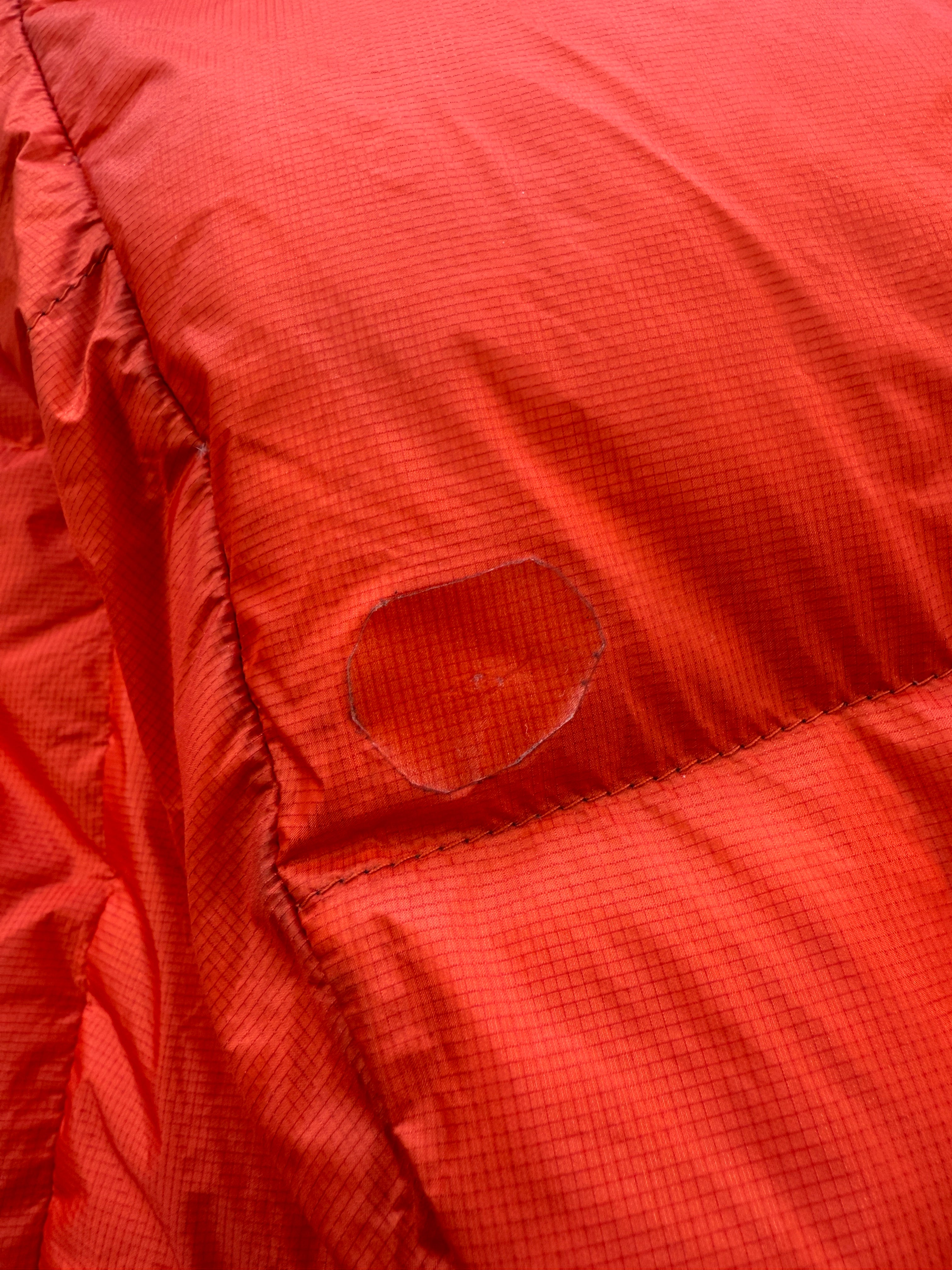 Orange down insulated jacket by Mountain Hardwear with a visible repair patch.