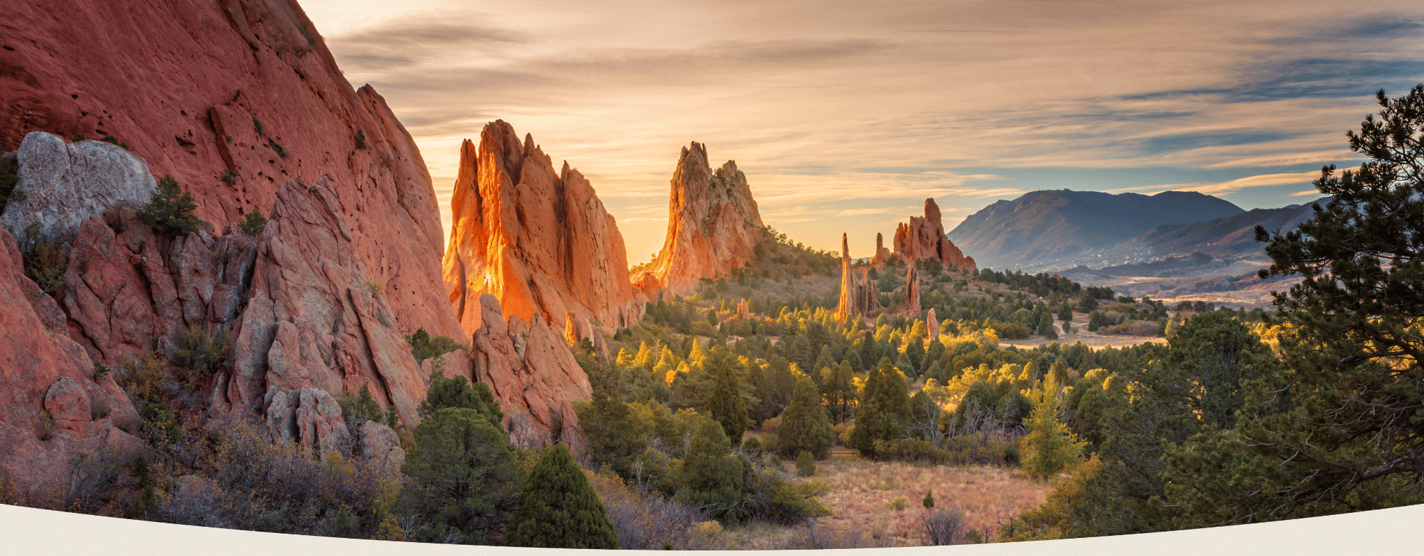 Sunset over rocky landscape with trees and mountains in the distance