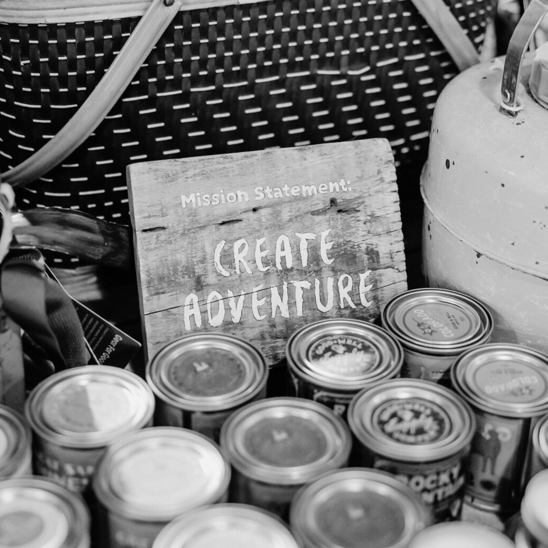 Wooden sign with 'Mission Statement: Create Adventure' surrounded by candles.