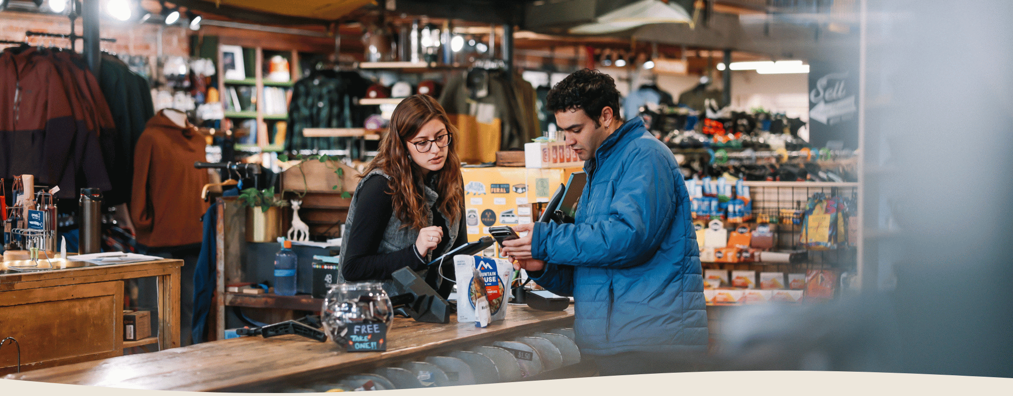 Two people at a counter in a store with shelves and products in the background